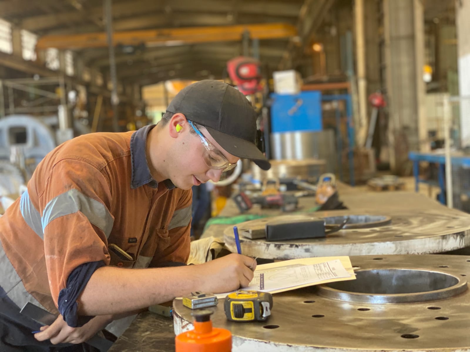 ABC tradesman performing quality-assurance measurement on a large machined circular flange