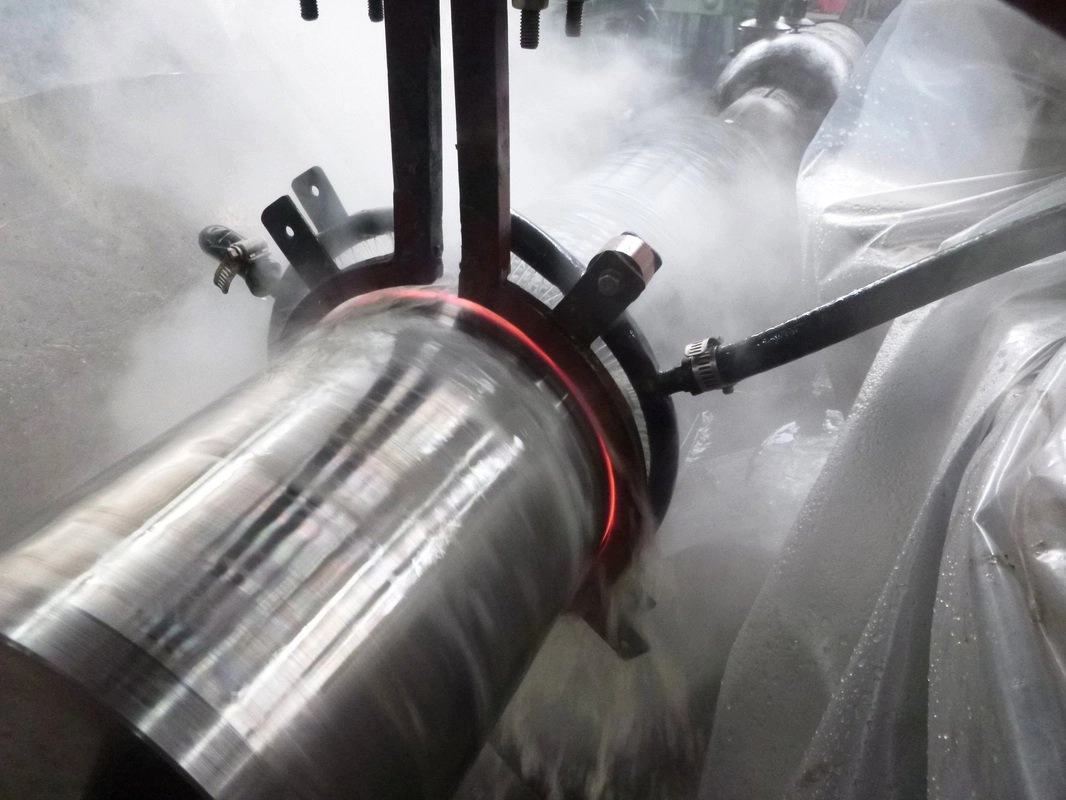 Induction hardening in progress, red heat glowing on a rotating shaft amid steam